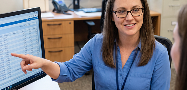 Medical Billing Specialist Pointing to Billing Code Data On-screen While Consulting with a Colleague.