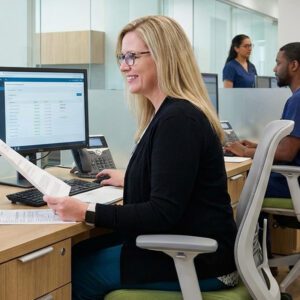 Medical Credentialing Specialist Comparing a Printed Remittance Document to a Claims List on Her Computer Screen